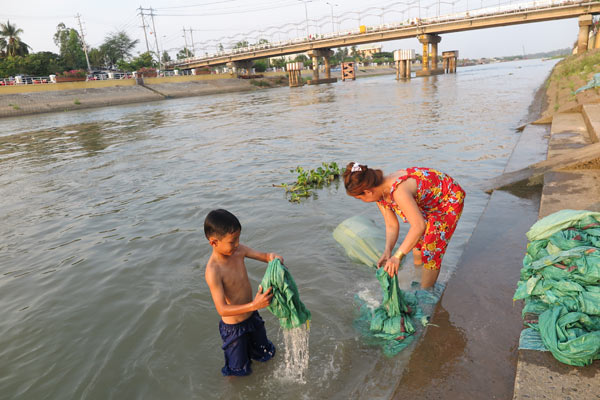 A woman and her son wash bags in the Mekong River on Monday. Photos by Xinhua, Wang Jian / China Daily and provided to China Daily